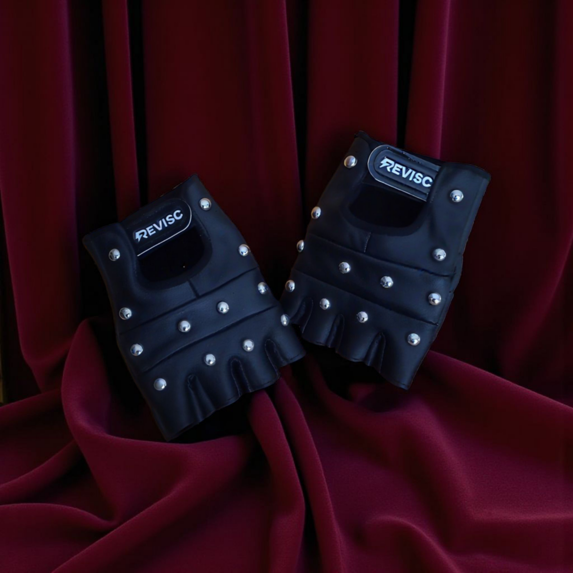 Pair of black fingerless gloves with silver studs on a red fabric background